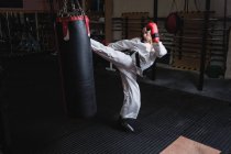 Esportivo Mulher praticando karatê com saco de perfuração no estúdio de fitness — Fotografia de Stock