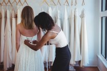 Mujer probándose el vestido de novia con la ayuda del diseñador de moda en el estudio - foto de stock