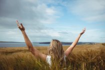 Rear view woman standing with raised hands in field — Stock Photo