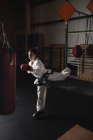 Sportlerin übt Karate mit Boxsack im dunklen Fitnessstudio — Stockfoto