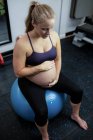 Беременная женщина, сидящая на мяче в спортзале — стоковое фото