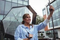 Bella donna che tiene l'ombrello mentre prende selfie durante la stagione delle piogge — Foto stock