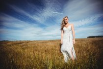 Задумчивая женщина, стоящая на пшеничном поле в солнечный день — стоковое фото