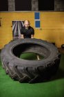Desportista bonito levantando pneu pesado no ginásio — Fotografia de Stock