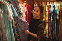 Портрет усміхненої жінки, яка вибирає одяг на вішалках в магазині одягу — стокове фото