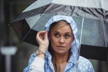 Mujer pensativa sosteniendo paraguas durante el tiempo lluvioso - foto de stock