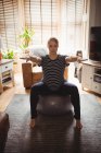 Вид спереду Вагітна жінка виконує розтяжку вправи на фітнес-кулі у вітальні вдома — стокове фото