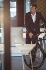 Homme d'affaires debout avec un vélo dans le bureau — Photo de stock