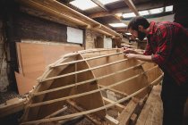 Mann misst Holzplanke in Bootswerft — Stockfoto