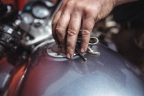 Рука механика закрывает топливный бак мотоцикла в цехе — стоковое фото