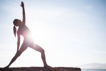 Frontansicht einer Frau, die an sonnigen Tagen Yoga auf Treibholz macht — Stockfoto