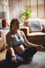 Femme enceinte effectuant du yoga dans le salon à la maison — Photo de stock
