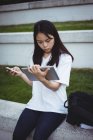 Молодая женщина с помощью мобильного телефона и цифрового планшета в саду — стоковое фото