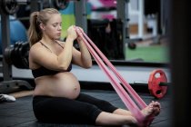 Mujer embarazada haciendo ejercicio con banda de resistencia en el gimnasio - foto de stock