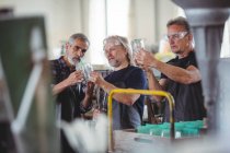 Sopradores de vidro interagindo ao examinar vaso de vidro na fábrica de sopro de vidro — Fotografia de Stock