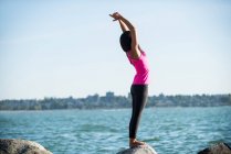 Vista lateral de Mujer realizando yoga sobre roca en día soleado - foto de stock