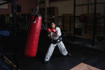 Woman in karate kimono practicing with punching bag in fitness studio — Stock Photo