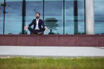 Businessman practicing yoga outside office building — Stock Photo