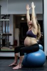 Pregnant woman performing stretching exercise on fitness ball in gym — Stock Photo