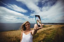 Smiling woman taking selfie with smartphone in field — Stock Photo