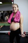 Portrait of pregnant woman lifting dumbbells in gym — Stock Photo