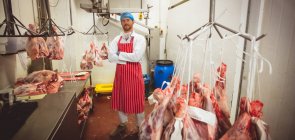Retrato de açougueiro de pé com os braços cruzados na sala de armazenamento de carne no açougue — Fotografia de Stock