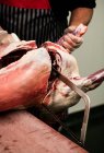 Sección media del carnicero que corta la canal de cerdo con una sierra en la carnicería - foto de stock