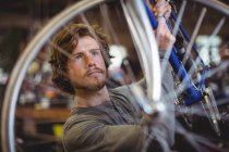 Mecánico examinando una rueda de bicicleta en taller - foto de stock