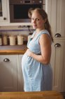 Retrato de la mujer embarazada de pie en la cocina en casa - foto de stock