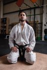 Человек в кимоно карате сидит на полу в фитнес-студии — стоковое фото