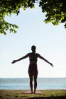 Vista posterior de la mujer realizando yoga en la costa en un día soleado - foto de stock