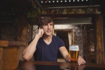 Homem falando no celular em bar com copo de cerveja na mão — Fotografia de Stock