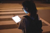 Вид сзади на молодую женщину с помощью цифрового планшета на улице ночью — стоковое фото
