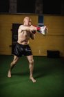 Tutta la lunghezza del boxer thailandese muscoloso senza camicia che pratica la boxe in palestra — Foto stock