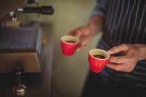 Mid section of waiter holding coffee cups at counter in workshop — Stock Photo