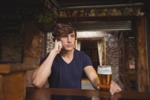 Мужчина разговаривает по мобильному телефону в баре со стаканом пива в руке — стоковое фото