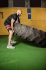 Vista lateral de belo desportista levantar pneu pesado no ginásio — Fotografia de Stock