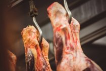 Primer plano de la carne roja pelada colgada en el almacén de la carnicería - foto de stock