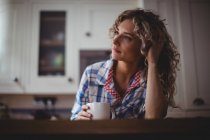 Mujer pensativa tomando café en la cocina en casa - foto de stock