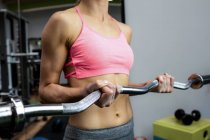 Sección media de la mujer haciendo ejercicio con barra en el gimnasio - foto de stock