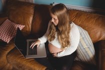 Vue grand angle de femme enceinte en utilisant un ordinateur portable dans le salon à la maison — Photo de stock