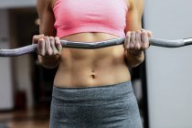Mid-section of woman working out with barbell at gym — Stock Photo