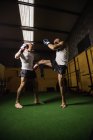 Vista de ángulo bajo de dos boxeadores tailandeses practicando boxeo en gimnasio - foto de stock