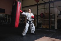Giovane donna che pratica karate con sacco da boxe in palestra — Foto stock