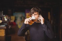 Чоловік розмовляє по мобільному телефону, маючи келих пива в барі — стокове фото