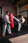 Longitud completa de hombre y mujer practicando karate con saco de boxeo en el estudio - foto de stock