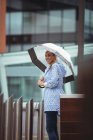 Hermosa mujer sosteniendo el paraguas y de pie en la calle durante el tiempo lluvioso - foto de stock