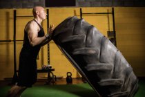 Side view of handsome sportsman lifting heavy tire in gym — Stock Photo