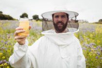 Apicultor segurando garrafa de mel no campo — Fotografia de Stock