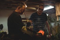 Team of glassblowers shaping blown glass piece with wet cloth at glassblowing factory — Stock Photo